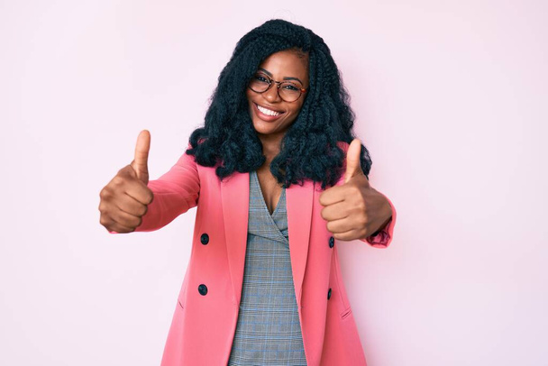 Schöne afrikanische Frau mit Businessjacke und Brille, die zustimmend positive Gesten mit der Hand macht, Daumen hoch lächelnd und glücklich über den Erfolg. Siegergeste.  - Foto, Bild