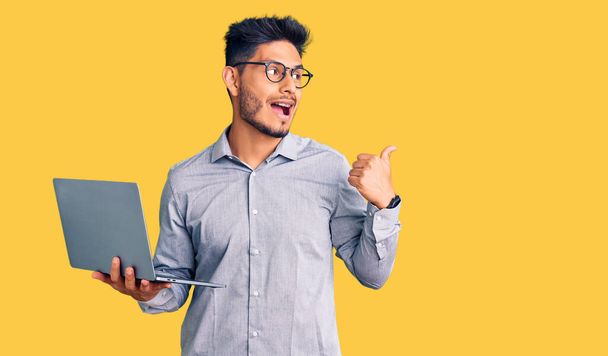 Handsome latin american young man working using computer laptop pointing thumb up to the side smiling happy with open mouth  - Φωτογραφία, εικόνα