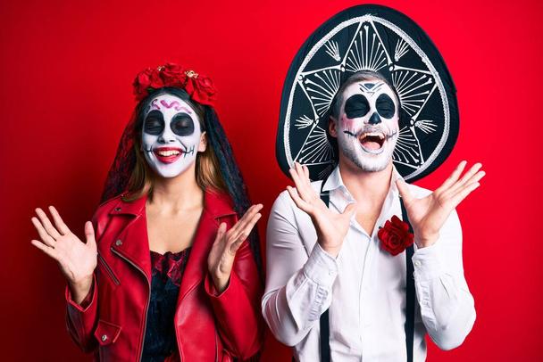 Couple wearing day of the dead costume over red celebrating mad and crazy for success with arms raised and closed eyes screaming excited. winner concept  - Fotoğraf, Görsel