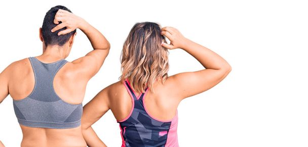 Een paar vrouwen die sportkleding achterstevoren dragen en met hand op hoofd aan twijfel denken  - Foto, afbeelding