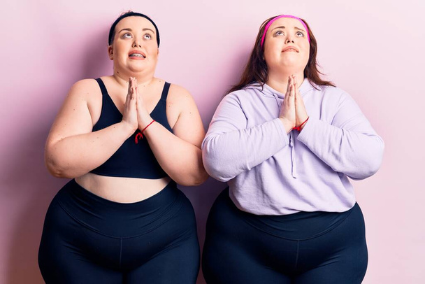 Young plus size twins wearing sportswear begging and praying with hands together with hope expression on face very emotional and worried. begging.  - Photo, Image