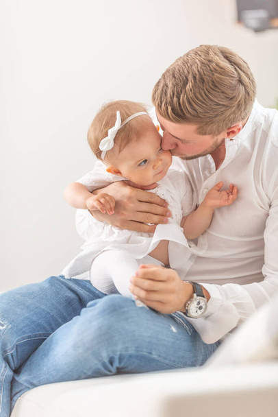 Young father holding and kissing his baby toddler girl on her cheek at home. - 写真・画像