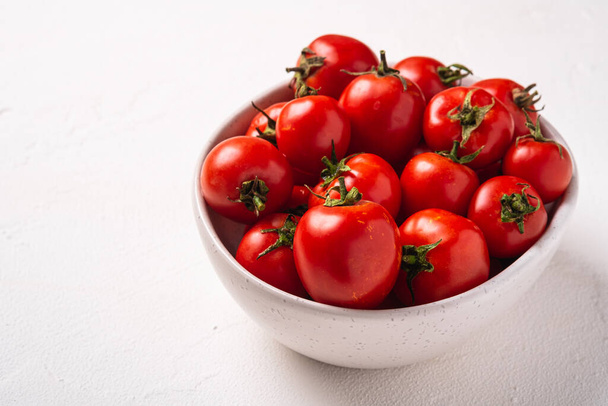 Fresh ripe tomatoes with water drops in bowl on white concrete background, angle view - Valokuva, kuva