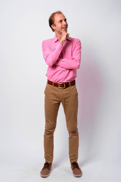 Studio shot van zakenman met blond haar dragen roze shirt tegen witte achtergrond - Foto, afbeelding