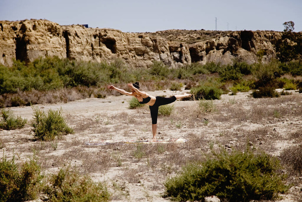 Young active woman practicing yoga in desert on sunny day, health and active life concept - Photo, Image
