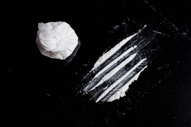 黒い背景のビニール袋に白い粉(ヘロイン、コカイン、麻薬)が散布され - 写真・画像