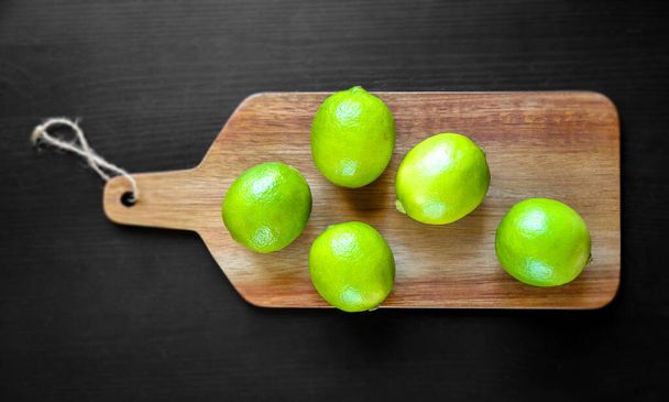Organic fresh limes on a wooden cutting board. Top view - Zdjęcie, obraz