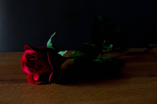 A selective focus shot of a beautiful red rose on a wooden surface with a black background - Φωτογραφία, εικόνα