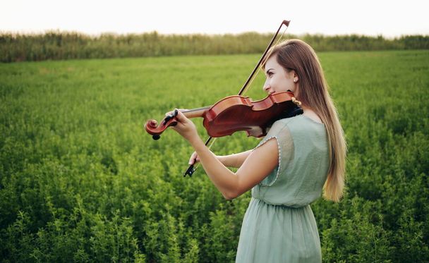 バイオリンを弾く緩やかな髪を持つロマンチックな女性。自然の中で日没の光。バイオリンの練習 - 写真・画像