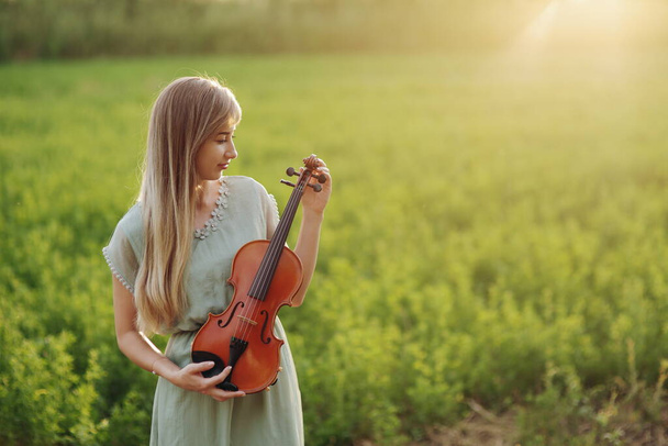 Violoniste musicienne tenant un violon dans ses mains à la lumière du coucher du soleil. Concept de formation violon - Photo, image