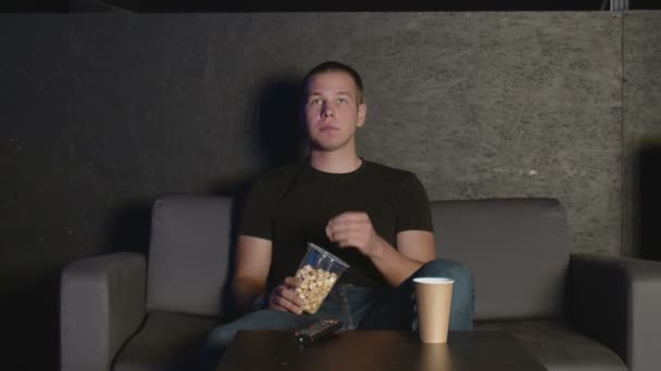 Knappe man die popcorn eet en thuis tv kijkt met afstandsbediening ontspannen op de bank - Video