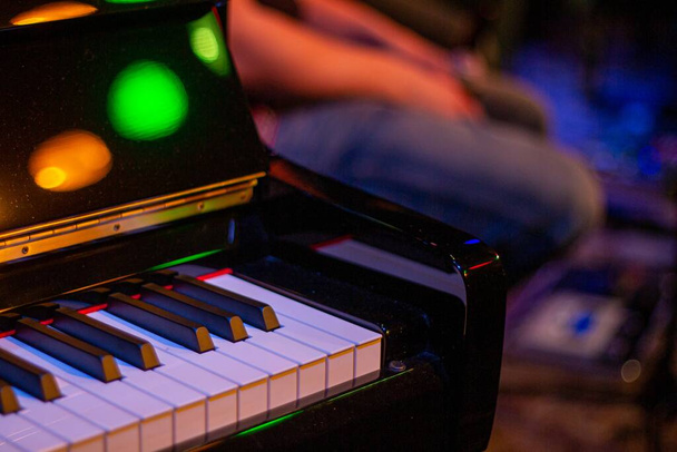 A closeup shot of the corner of a piano with colorful lights around - Foto, Imagen