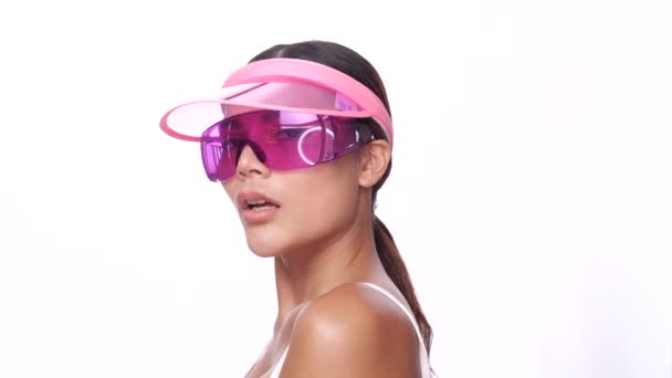 Retrato hermosa mujer asiática en rosa sombrero de la visera del sol y gafas de sol posando, mirando a la cámara sobre fondo blanco - video en cámara lenta - Metraje, vídeo