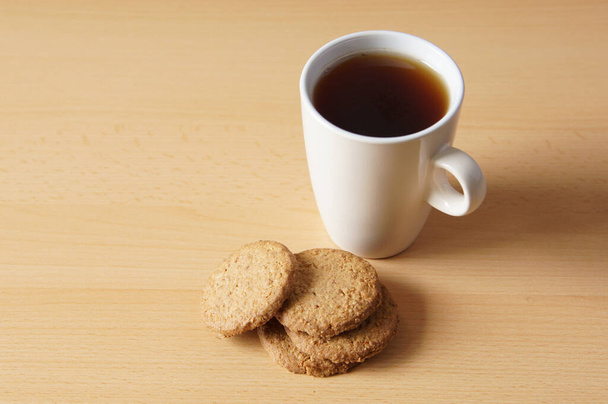 Eine Nahaufnahme der leckeren Kekse mit einer Tasse Kaffee auf einer Holzoberfläche - Foto, Bild