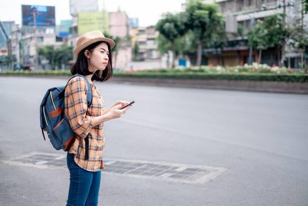 Aasian naisten turisti Stand soittaa taksin sovelluksen älypuhelimeen. Teknologia helpottaa hänen matkaansa. Matkustaessaan pääkaupungissa. - Valokuva, kuva