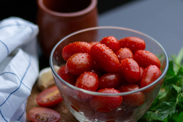 A closeup shot of a bowl of tomatoes next to greens - Фото, зображення