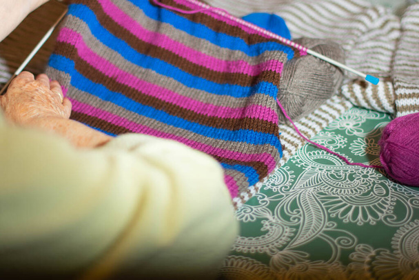 A close up shot of a grandmother knitting a sweater from colorful thread yarns - 写真・画像