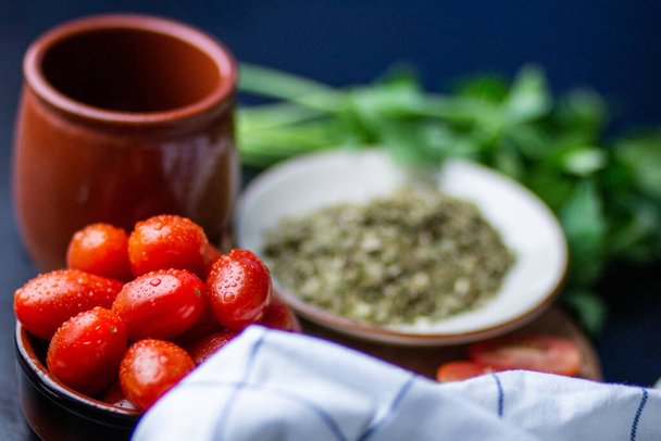 A closeup shot of a bowl of tomatoes next to a cup, a plate of condiment and greens - Foto, Imagen