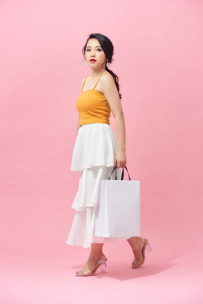Full length of young woman holding shopping bags and smiling while walking isolated over pink background. - Valokuva, kuva