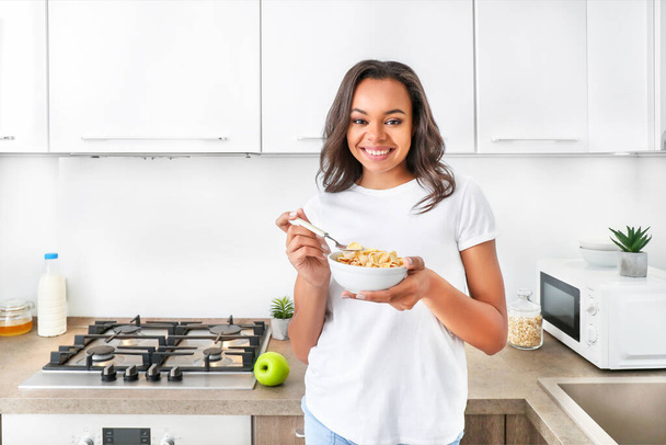 Young african woman eating corn flakes for breakfast in kitchen. - Foto, imagen