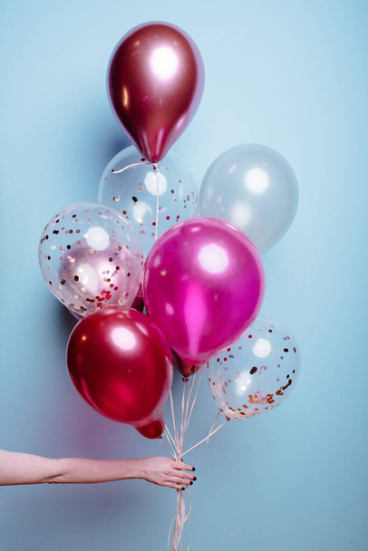 Composition of white, pink, transparent helium balloons in the hand of a woman on a blue background. - Foto, afbeelding