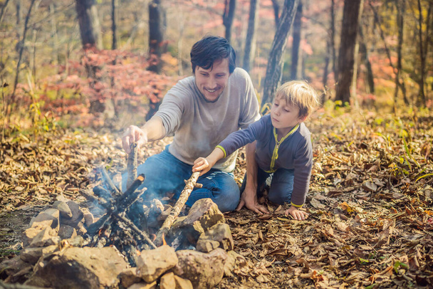 father and excited son sitting in tent in forest camping with bonfire - Photo, Image