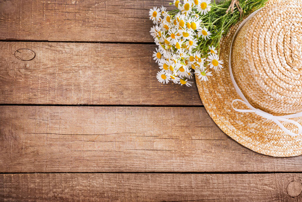 Chamomile bouquet and women's straw hat on wooden background. Top view. Copy space. - Foto, Bild