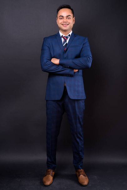 Студийный снимок молодого красивого индийского бизнесмена в синем костюме на черном фоне - Фото, изображение