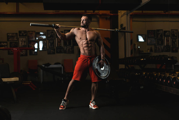 Atleta con cuerpo perfecto en pantalones cortos rojos en el gimnasio. luz suave - Foto, Imagen