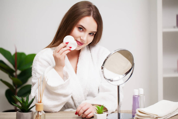 Souriante jeune femme se lave le visage avec une éponge de nettoyage du visage à la salle de bain - Photo, image