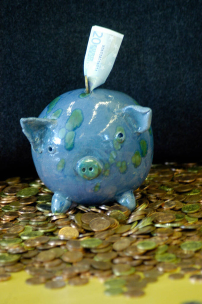 голубая и зеленая копилка с банкнотой, стоящей на столе, полном монет - Фото, изображение