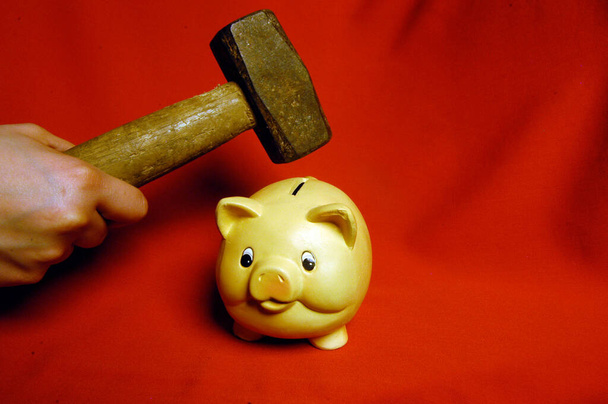 Zertrümmern eines Sparschweins mit einem Hammer, auf rotem Hintergrund - Foto, Bild