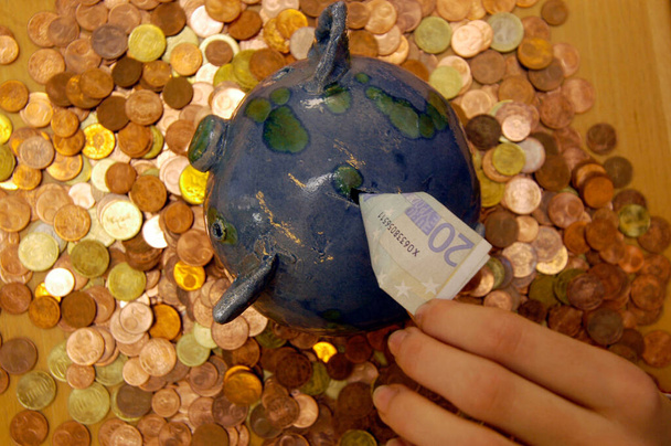 salvadanaio blu e verde con banconote in piedi su una scrivania piena di monete - Foto, immagini
