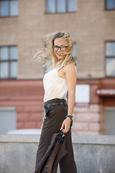 Beautiful young business woman with blond curly hair wearing a suit and glasses poses outdoors - Φωτογραφία, εικόνα