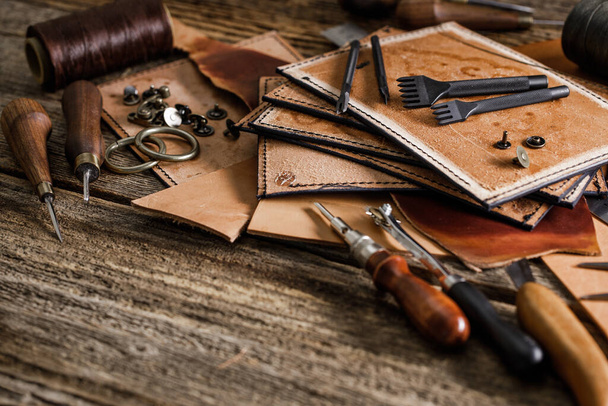 Leather craft tools on the old wood table in a shed. Leather craftsman workspace. Grounge dark wood texture background. - Fotó, kép