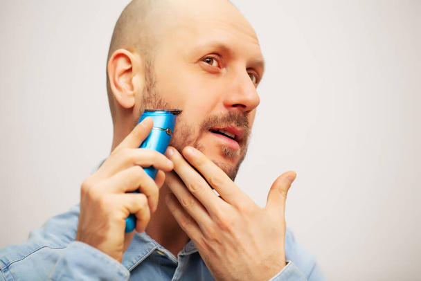 Hezký mladý vousatý muž stříhání vousy s trimmer - Fotografie, Obrázek