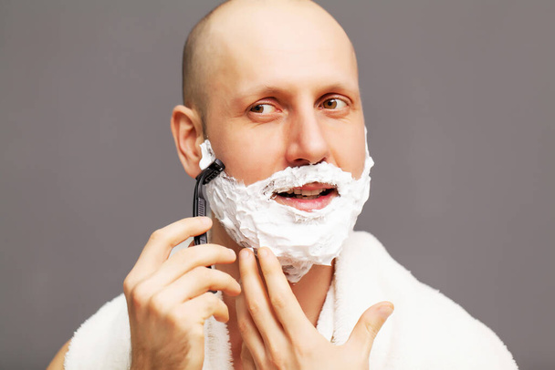 Портрет красивого чоловіка, що голиться за допомогою бритви і дивиться вбік
 - Фото, зображення