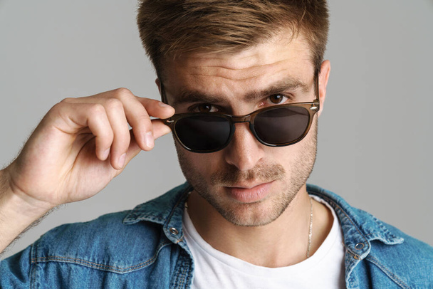 Portrait of handsome confident man in sunglasses posing and looking at camera isolated over grey background - Φωτογραφία, εικόνα