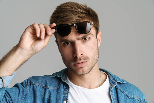 Portrait of displeased bold man in sunglasses posing and looking at camera isolated over grey background - Photo, Image