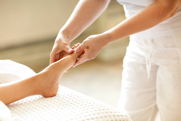 Nierozpoznawalny terapeuta korzystający z pliku stóp do masażu anonimowego klienta podczas pracy w salonie spa - Zdjęcie, obraz