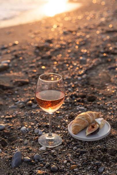 Бокал розового вина на пляже на закате. - Фото, изображение