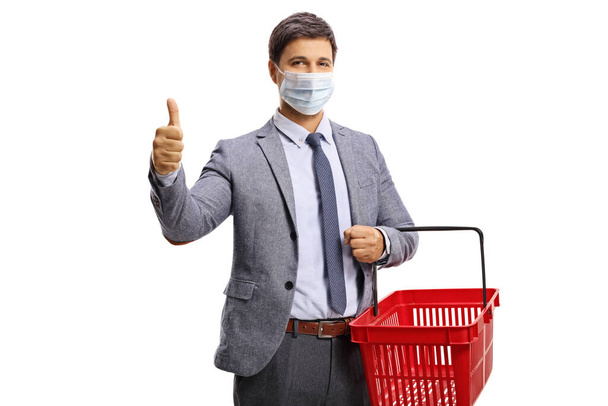 Man with a shopping basket showing thumbs up and wearing a protective face mask isolated on white background - Foto, Imagem