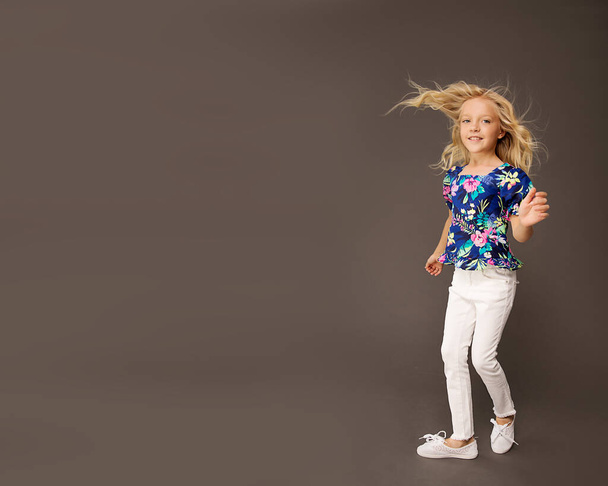 Маленькая симпатичная девочка блондинка с длинными волосами, девочка 7-8 лет в яркой летней одежде, танцующая на черном фоне, детский студийный портрет. День матери, семья любви, концепция детства - Фото, изображение
