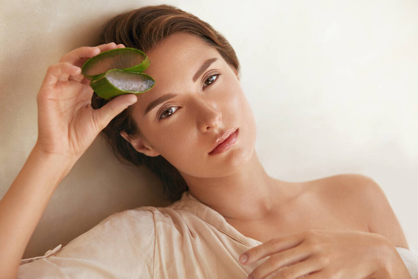 Aloe Vera. Woman Holding Slices Of Leaf And Looking At Camera. Beauty Portrait Of Tender Model With Natural Makeup, Radiant, Hydrated And Glowing Facial Skin. - Zdjęcie, obraz