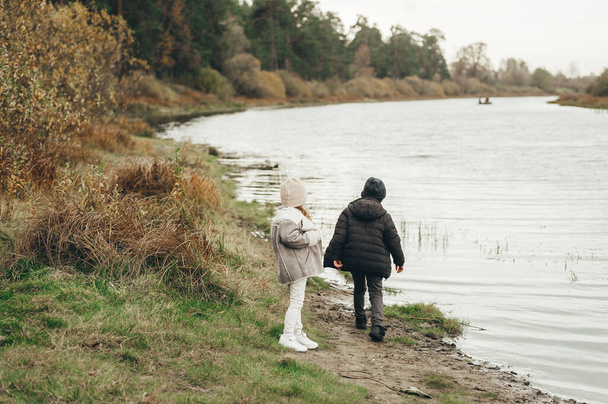 Kaksi söpöä lasta pitää hauskaa joen tai järven rannalla syyspäivänä. Lapset leikkivät veden äärellä. Perheaktiviteetit ulkona syksyllä. - Valokuva, kuva