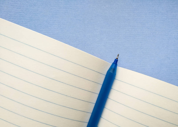 In Großaufnahme liegt ein blauer Stift in der Mitte eines offenen Notizbuchs in einer Reihe. Schulheft in Reihe für Notizen mit Kopierplatz. Schreibwaren für Schule und Büro. - Foto, Bild