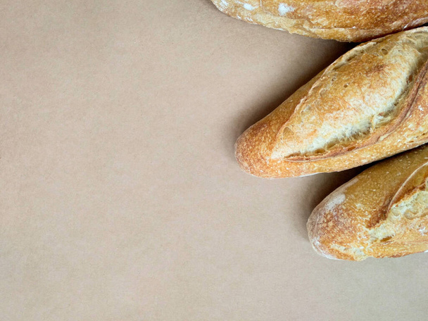Three fresh crunchy french baguettes on a beige background with place for text. Fresh bakery. Crispy bread for breakfast. Delicious picnic bread. Freshly baked baguette. - Photo, Image