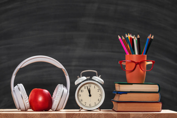 Back to school. Student set. Stack of books pencils glasses alarm clock headphones apple on the background of the black board. Education concept. - Фото, изображение