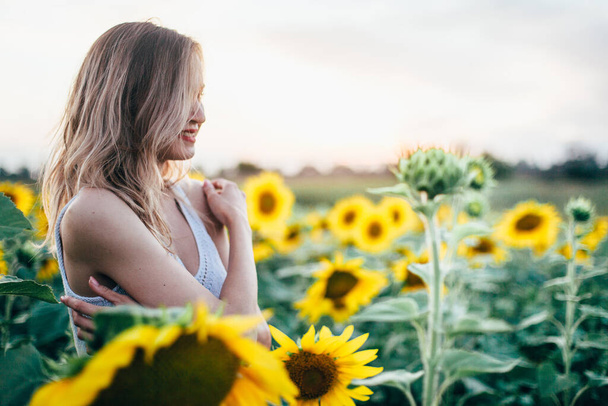 Young, slender girl in a white T-shirt poses at sunset in a field of sunflowers - Photo, image