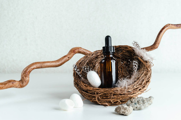 Bottle with face serum on white background. Place for  text. Essence for mature skin stands on  nest.  Silkworm cocoon for facial cleansing. Trends in cosmetology - Photo, Image
